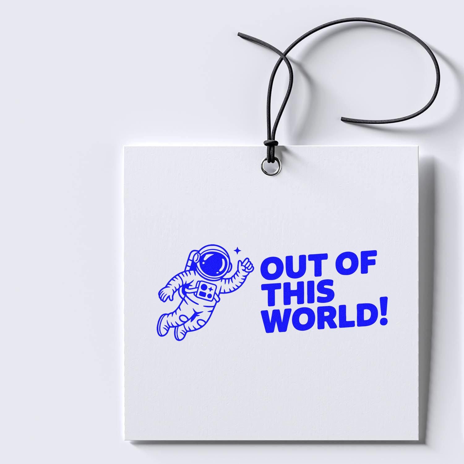 Space-themed rubber stamp design with astronaut and Out of This World! on a white gift tag for packaging and crafts.