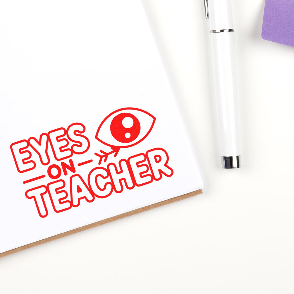 Eyes on Teacher rubber stamp impression on paper beside a pen, ideal for classroom behavior notes and teacher feedback.