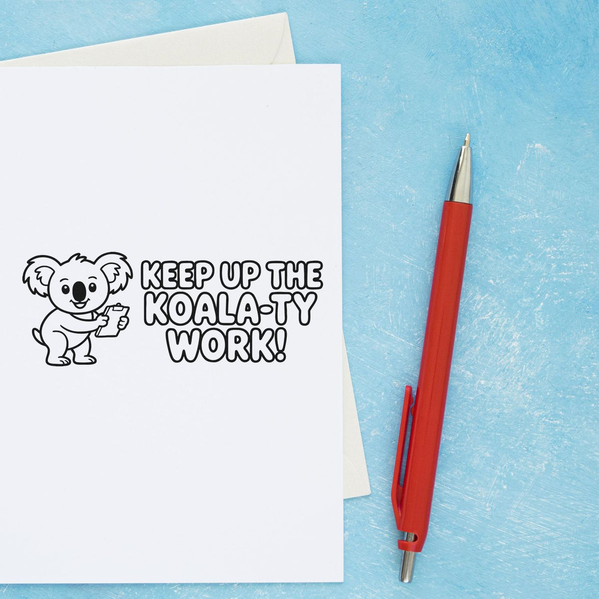 Koala rubber stamp with Keep Up the Koala-ty Work! motivational message on paper beside a red pen.