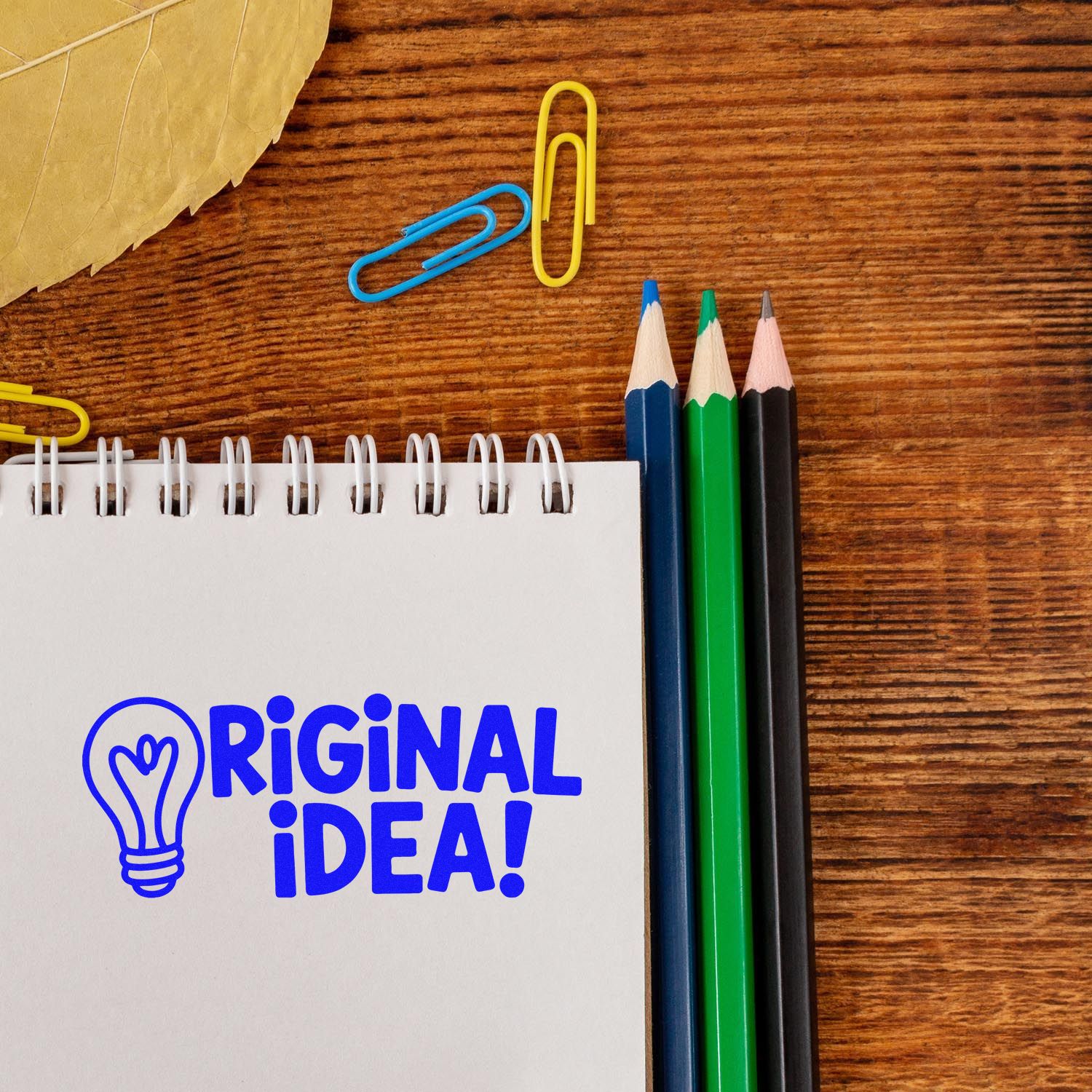 Original idea rubber stamp on notebook with pencils and paper clips on a wooden desk, creative office stationery concept