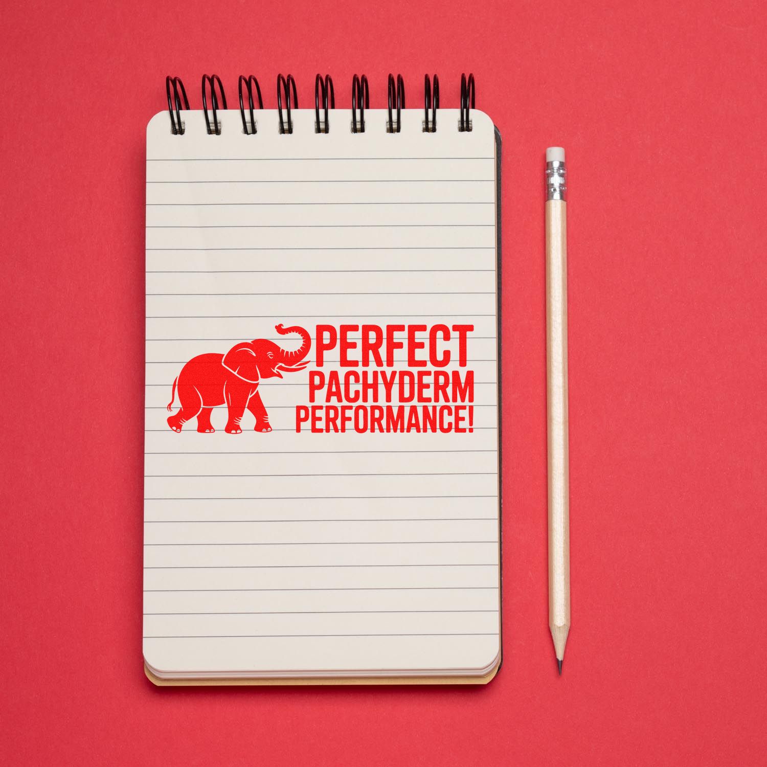 Custom rubber stamp with red elephant and Perfect Pachyderm Performance stamped on a lined notebook beside a pencil.
