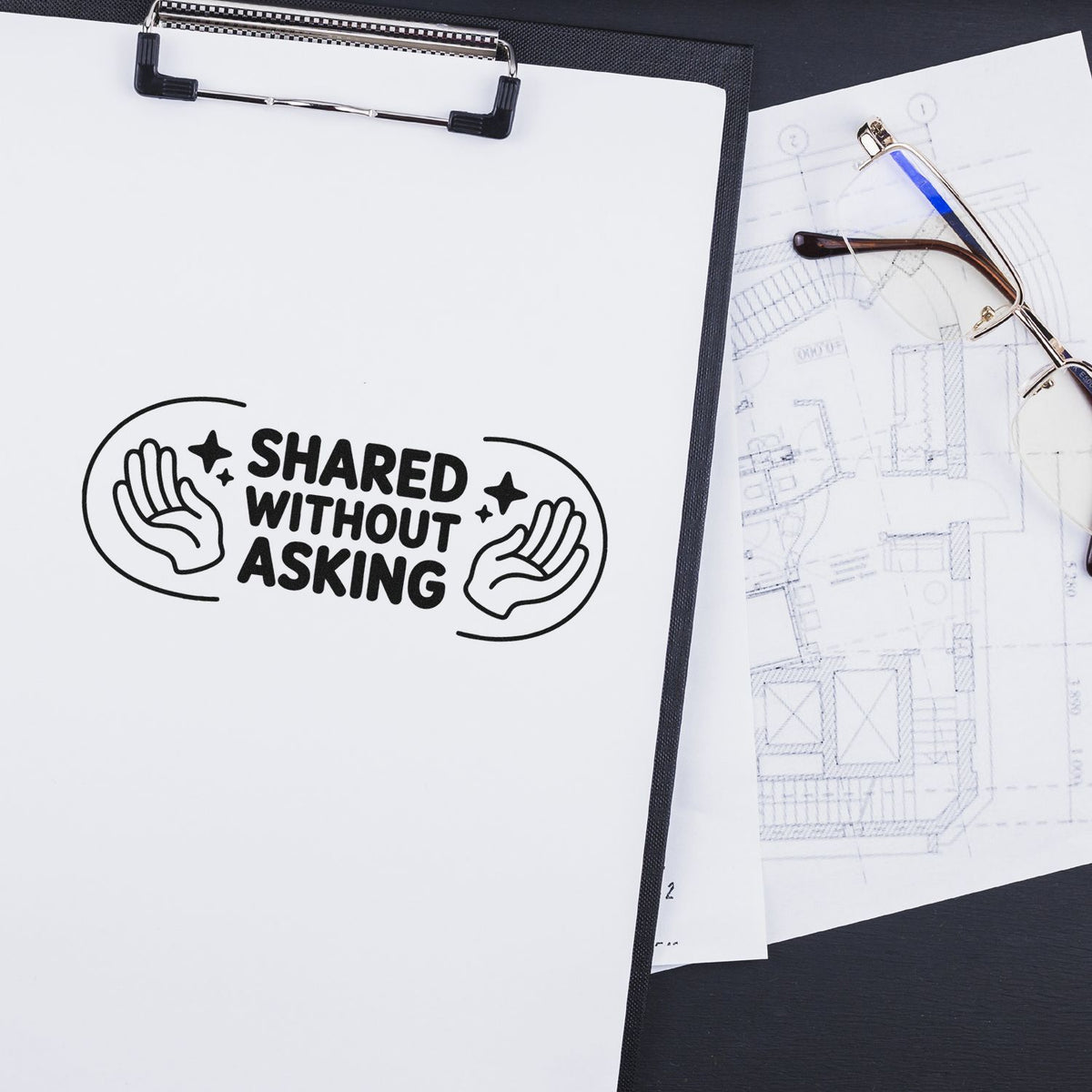 Custom rubber stamp design reading Shared Without Asking on a clipboard, with blueprint sketches and eyeglasses nearby.