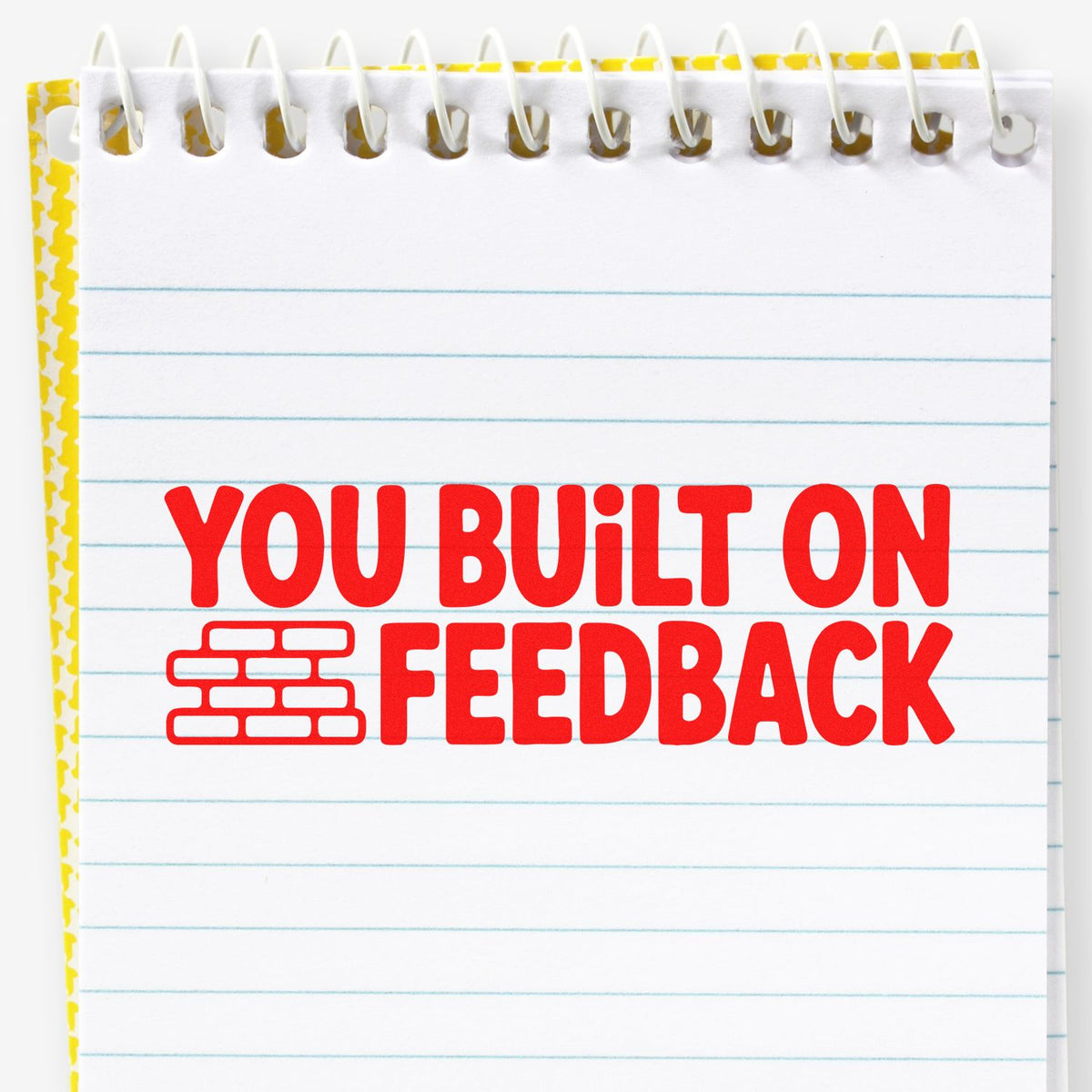 Custom rubber stamp design reading You Built on Feedback with brick icon on a lined notebook page.