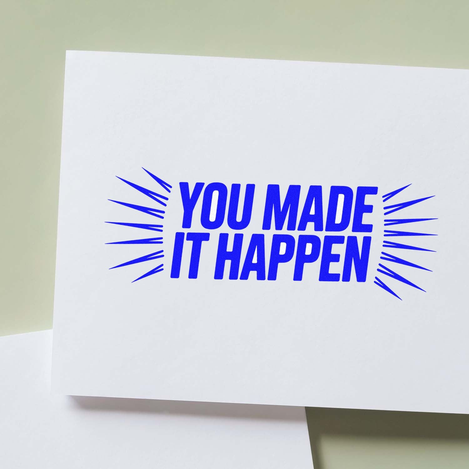 Blue custom rubber stamp design reading You Made It Happen with burst lines on white paper.