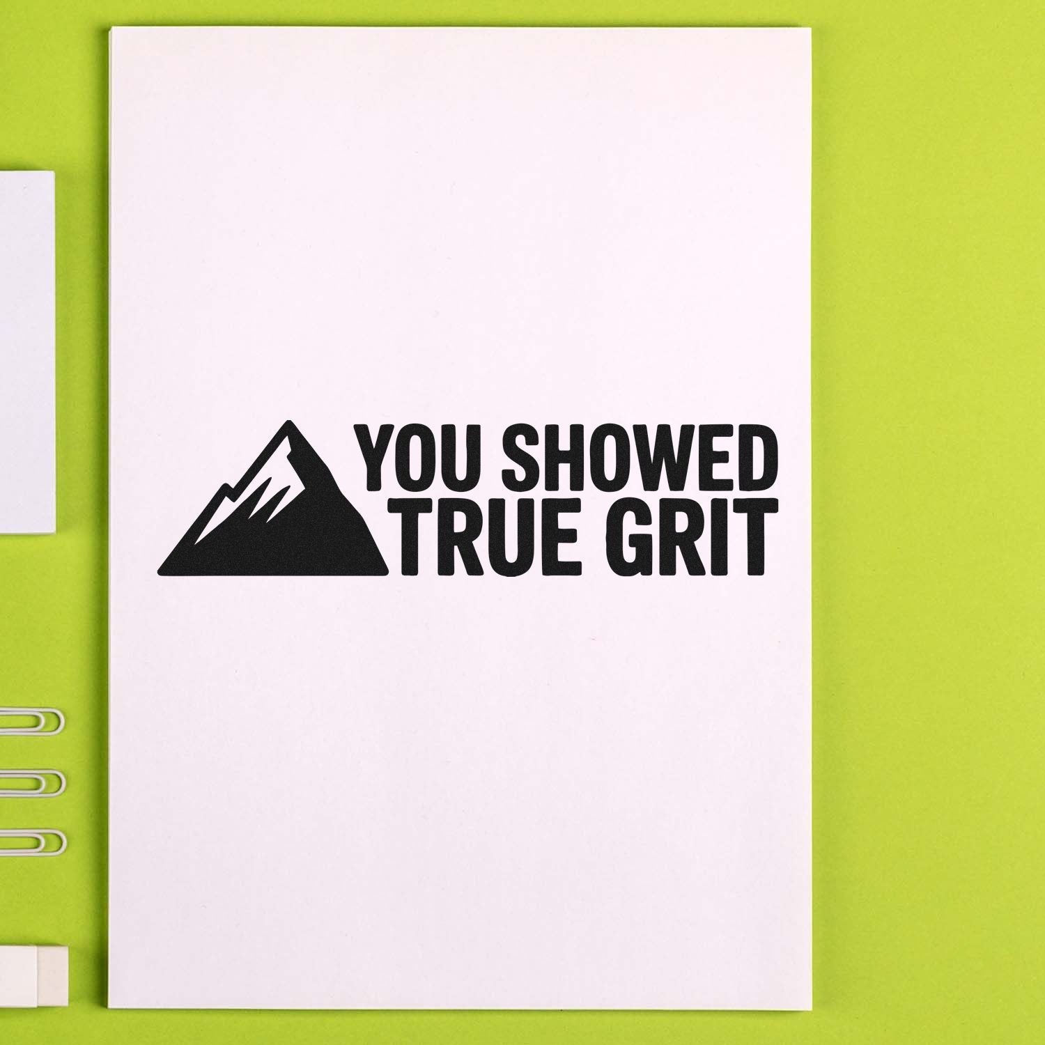 Motivational rubber stamp with mountain icon and "You Showed True Grit" message on white paper.