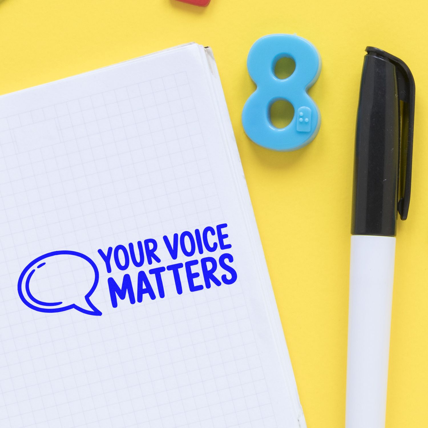 Custom rubber stamp imprint reading Your Voice Matters on notebook with speech bubble, beside a marker and number 8.