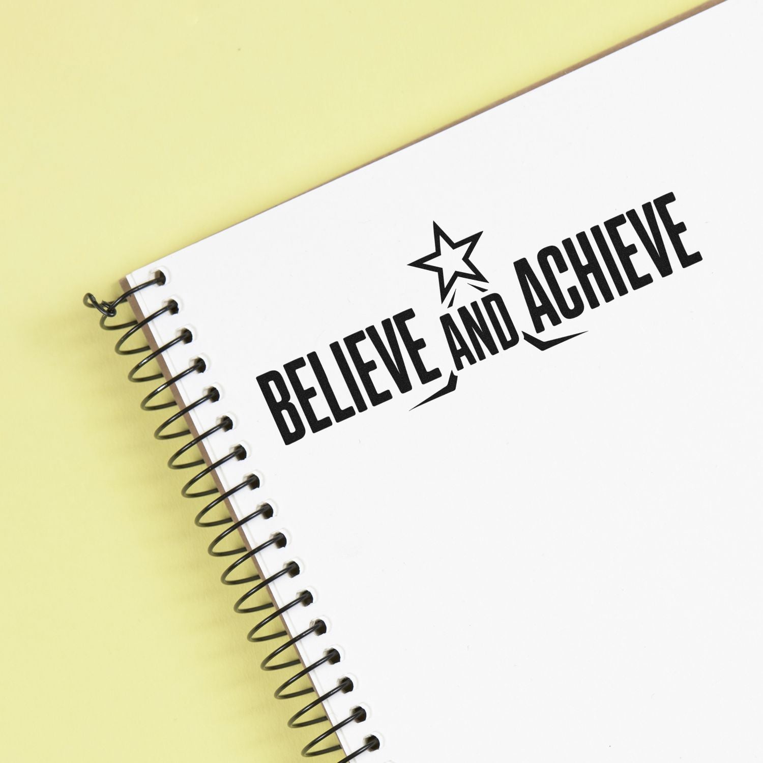 Motivational rubber stamp imprint reading Believe and Achieve on a spiral notebook cover.