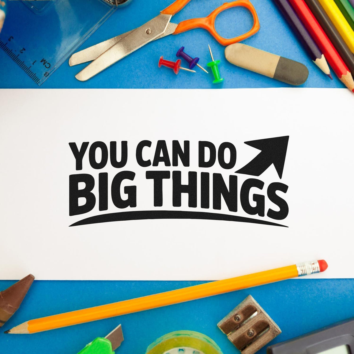 Motivational rubber stamp design reading You Can Do Big Things with school supplies on a blue desk background.
