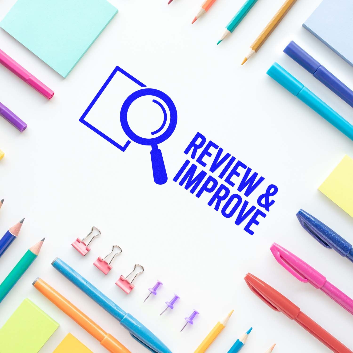 Review & Improve rubber stamp design with magnifying glass icon, surrounded by colorful stationery for office branding.