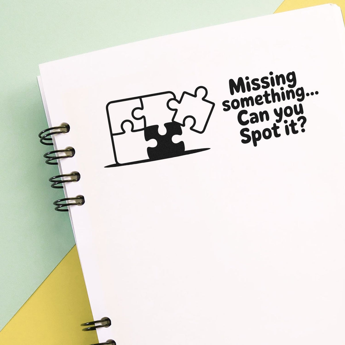 Custom rubber stamp with puzzle piece design and text Missing something... Can you spot it? on a notebook page.