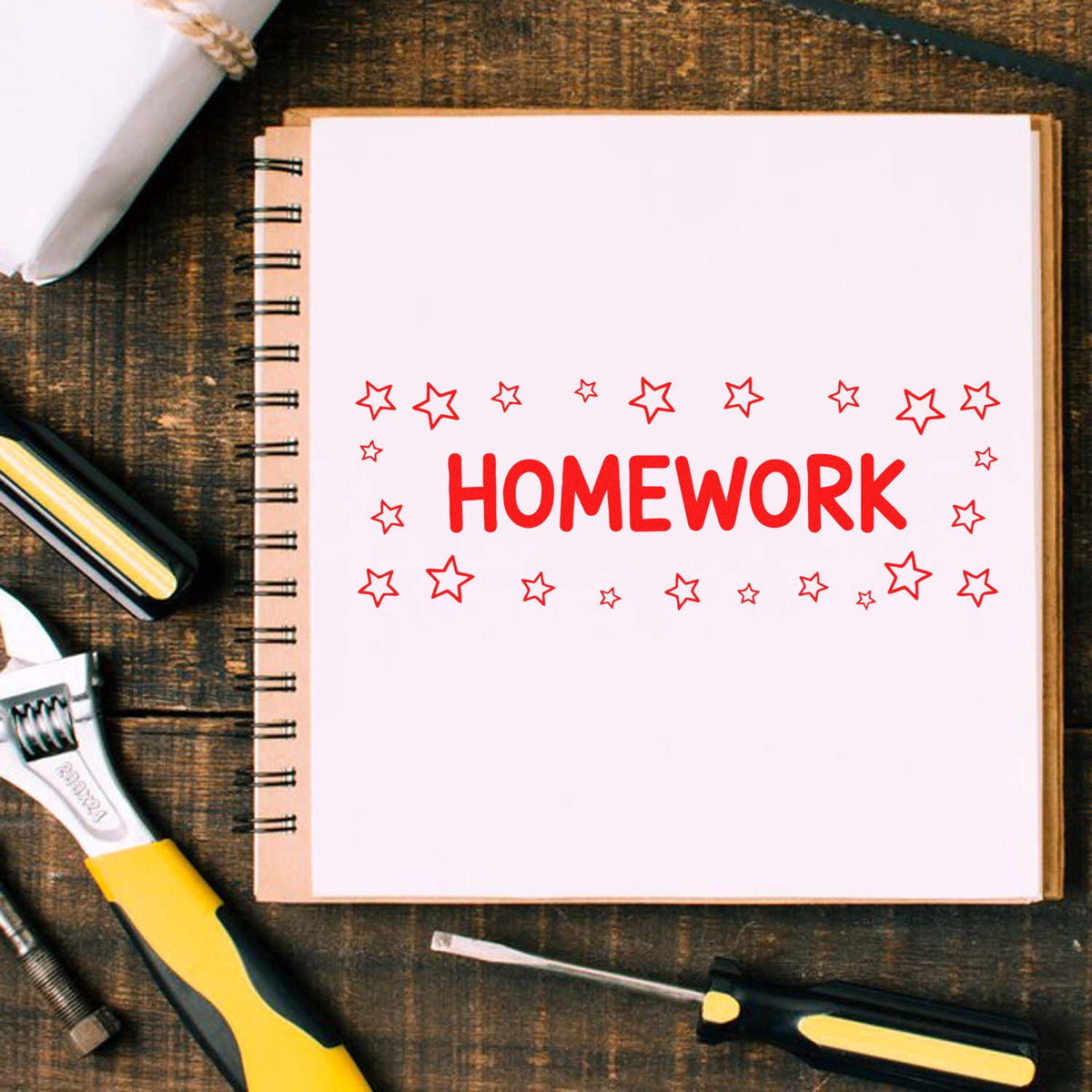 Homework rubber stamp design on a notebook page with stars, surrounded by school supplies and tools on a wooden desk.