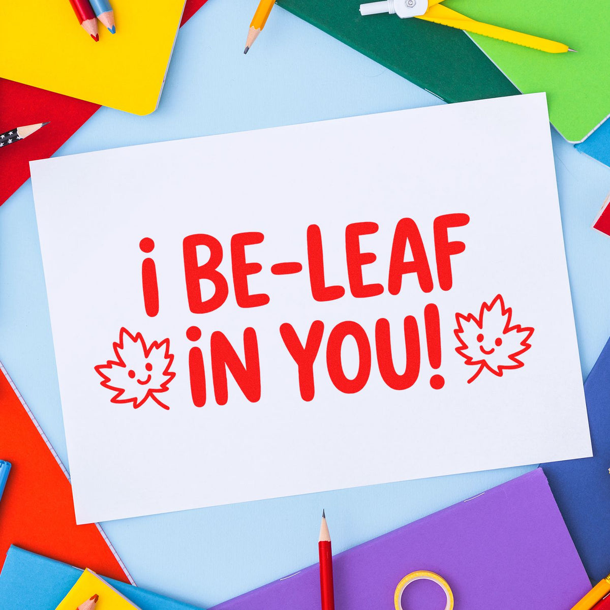 Custom rubber stamp design reading I Be-Leaf in You! on a white card with colorful stationery.