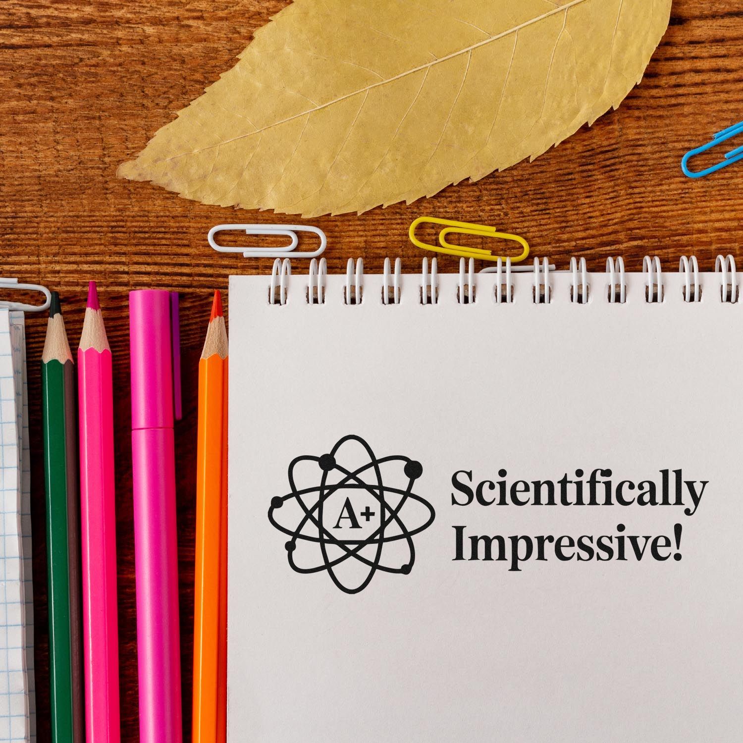 Scientifically Impressive! A+ atom rubber stamp on notebook, ideal for teacher grading and science-themed classroom use.