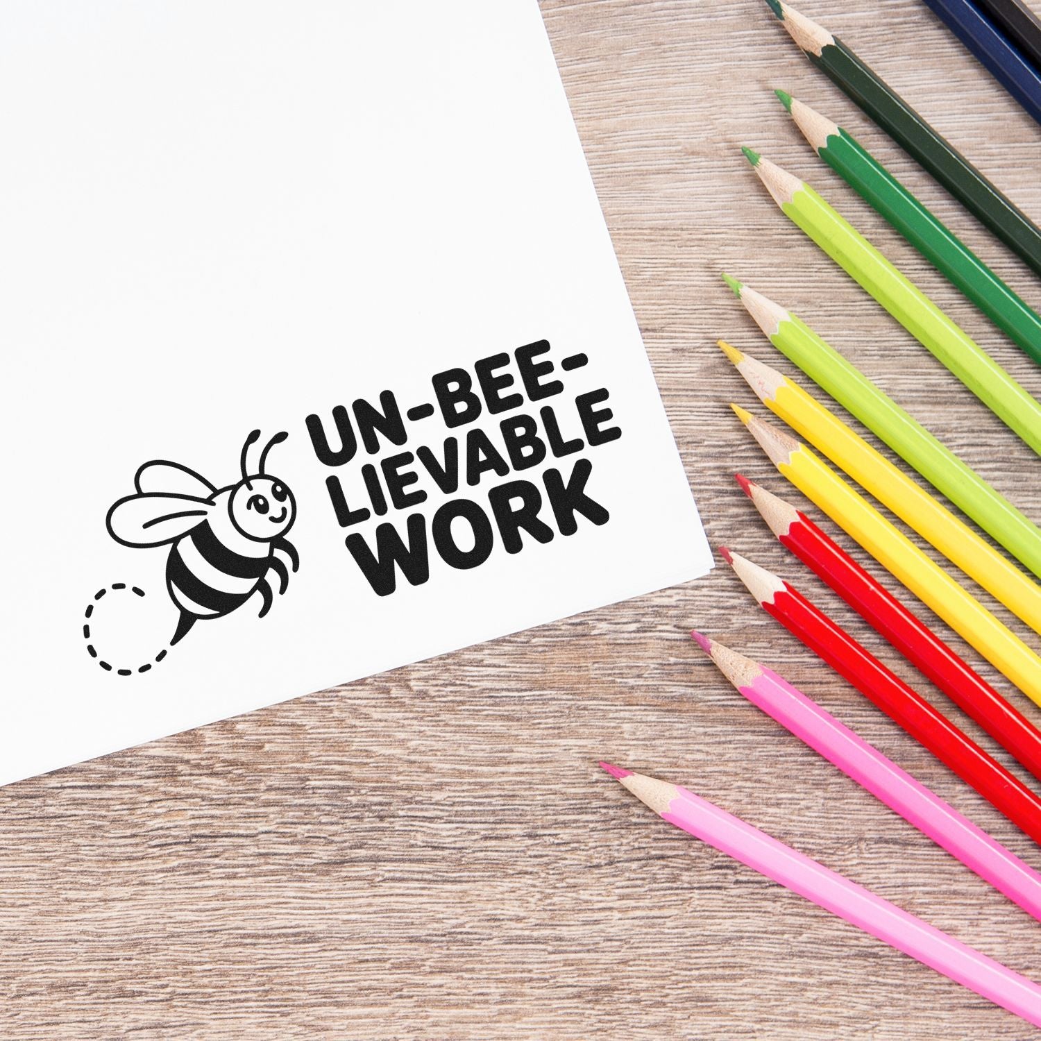 Bee-themed rubber stamp reading Un-bee-lievable Work for student praise, shown with colored pencils.