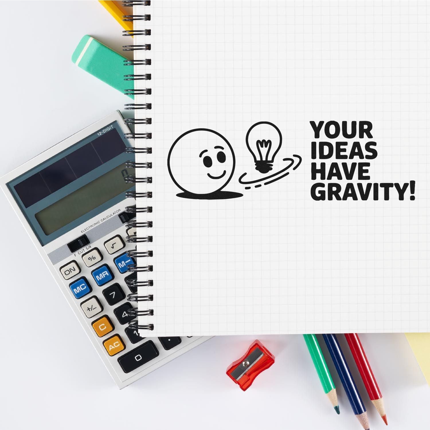 Motivational rubber stamp design reading Your Ideas Have Gravity! with smiley face and lightbulb on a notebook.