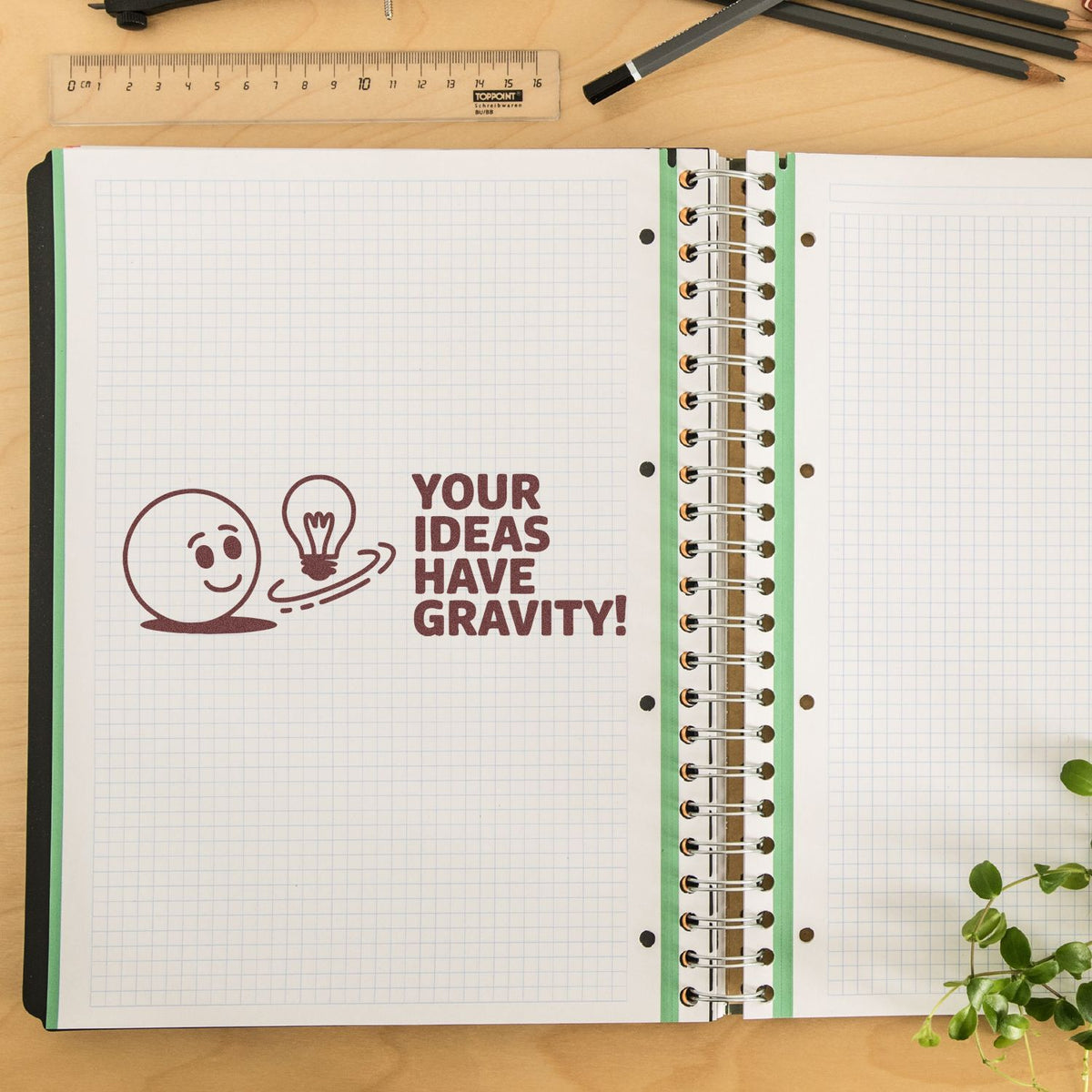 Custom rubber stamp impression reading Your ideas have gravity! on an open notebook, ideal for creative stationery branding.