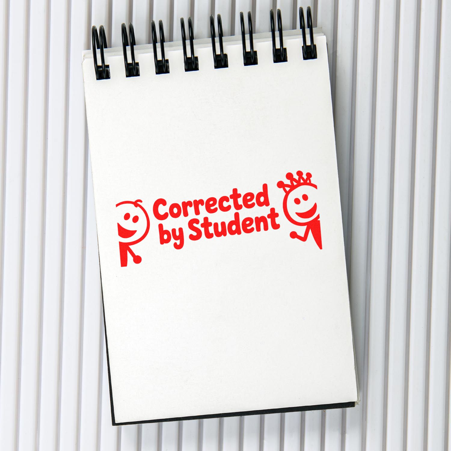 Red rubber stamp reading Corrected by Student on a spiral notebook, ideal for teacher grading and classroom use.