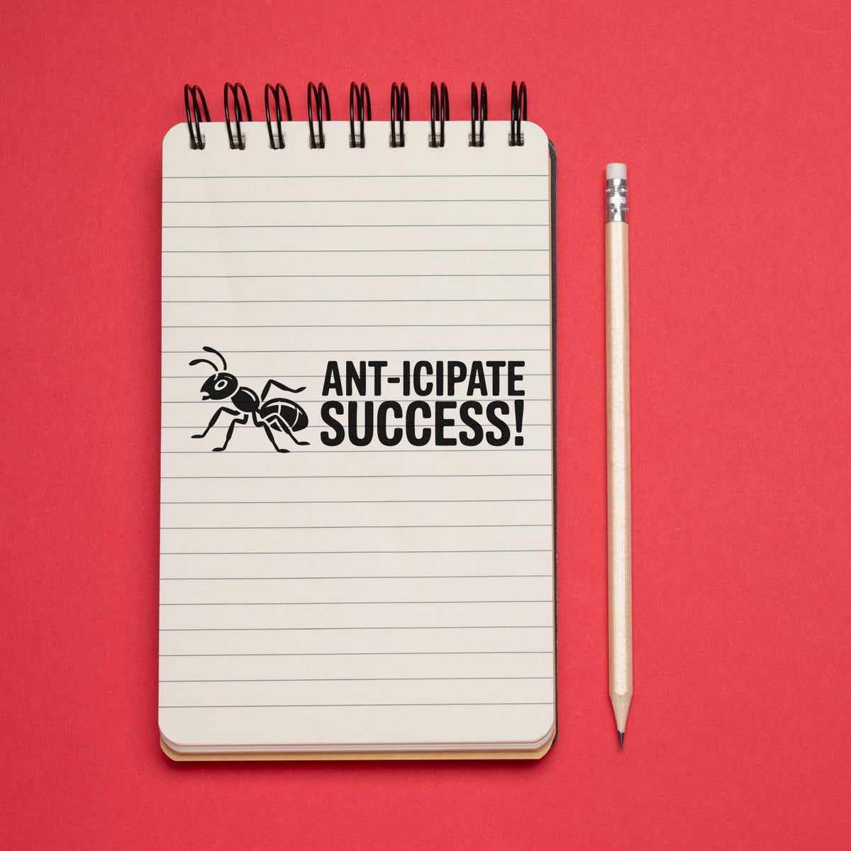 Anticipate Success ant rubber stamp imprint on lined notebook with pencil, creative office stationery on red background.