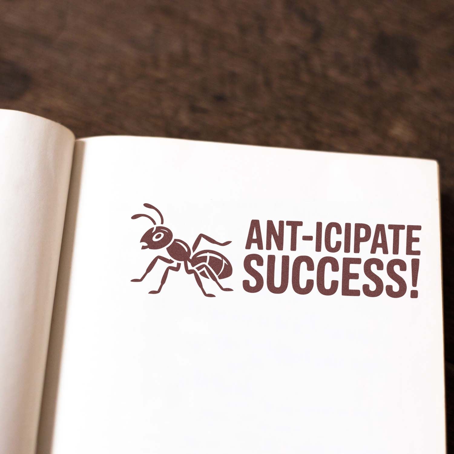 Rubber stamp impression reading Ant-icipate Success! with ant graphic on an open notebook page.