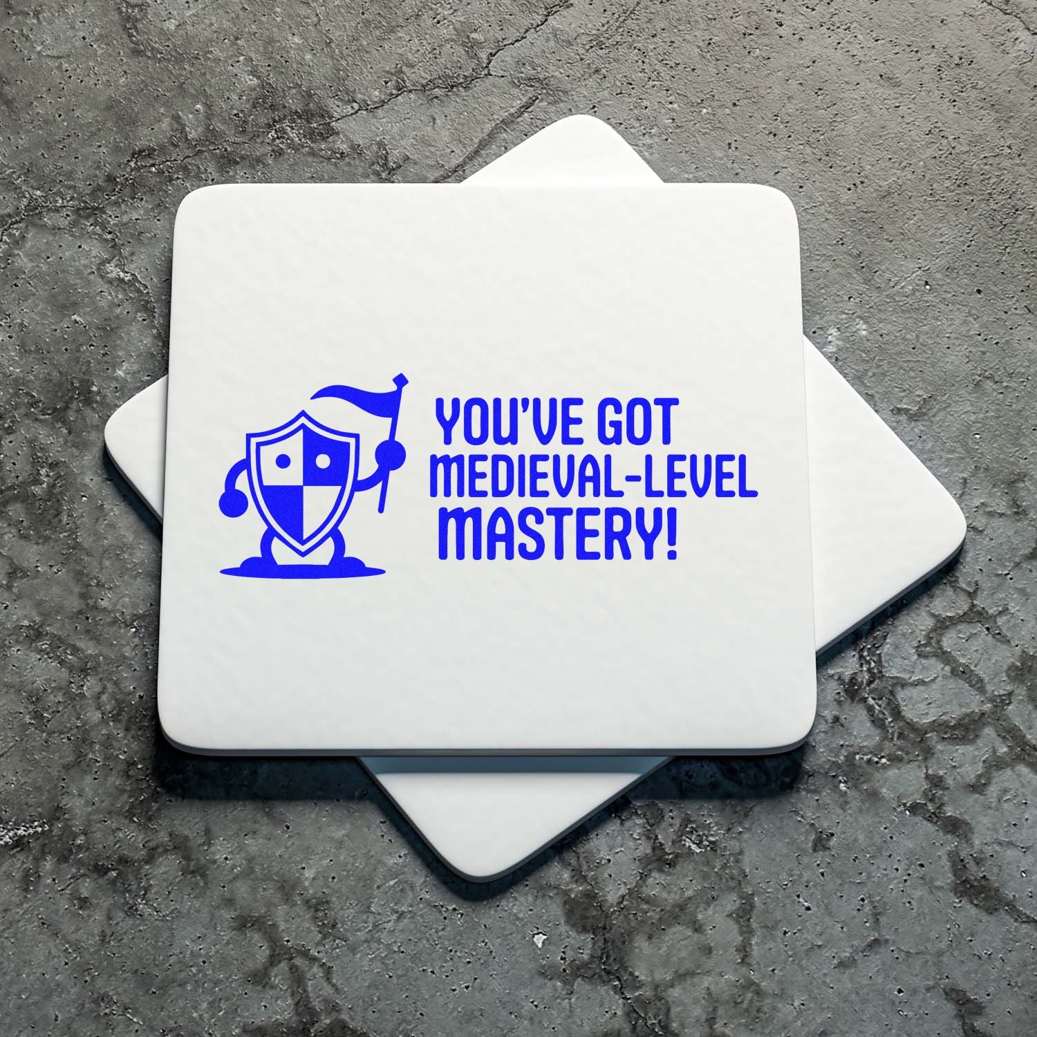 Medieval-themed custom rubber stamp with shield character and Youve got medieval-level mastery! on white square coaster.