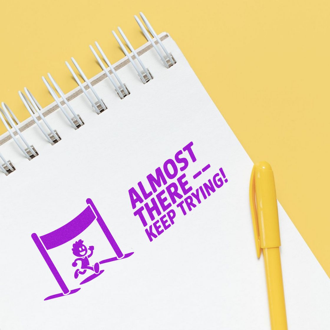 Motivational rubber stamp design with Almost ThereKeep Trying! and runner finish-line icon on a notebook.