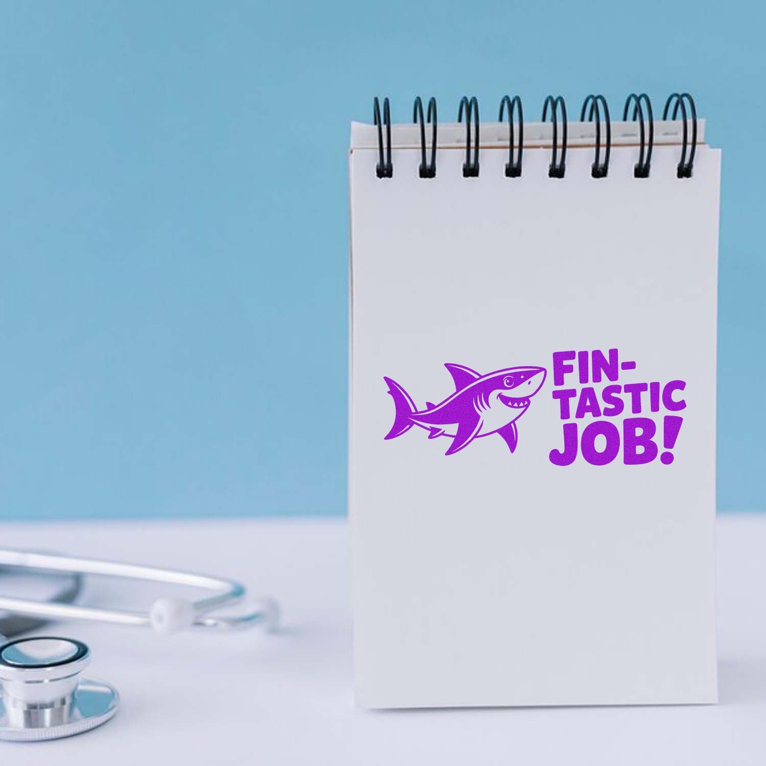 Purple shark Fin-tastic Job! rubber stamp on notepad, ideal motivational stamp for teachers, offices, and healthcare teams.