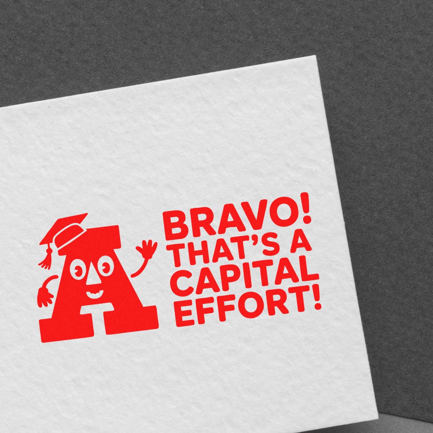 Red rubber stamp imprint reading Bravo! Thats a Capital Effort! with a graduation-cap letter A, ideal for classroom rewards.