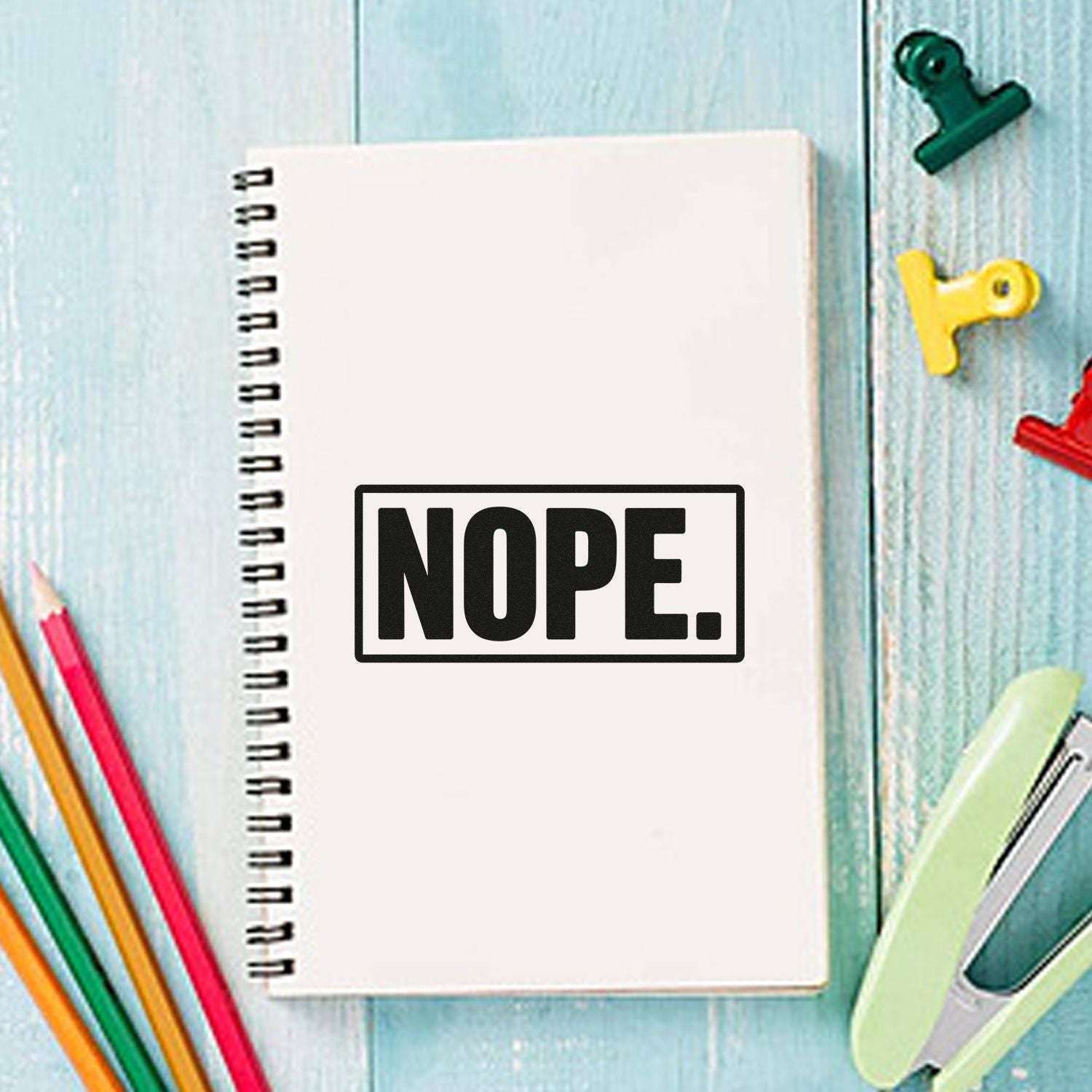 NOPE rubber stamp on spiral notebook with colorful stationery, perfect for office or craft labeling.