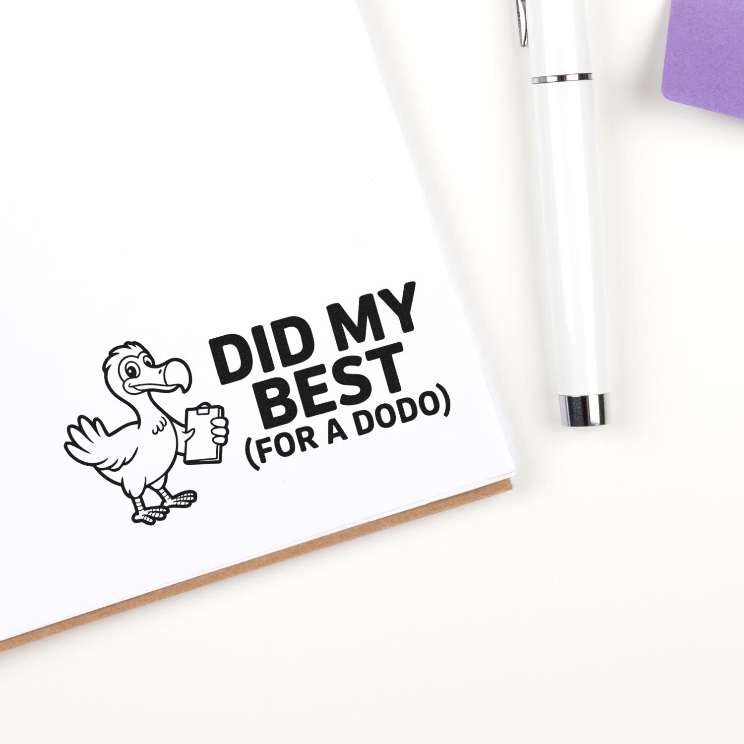 Dodo rubber stamp impression reading Did My Best (For a Dodo) on notebook page, with pen beside it.