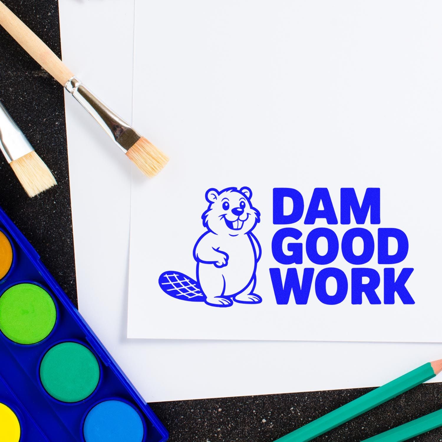 Dam Good Work rubber stamp with beaver design, displayed with paintbrushes and watercolor supplies for craft projects.