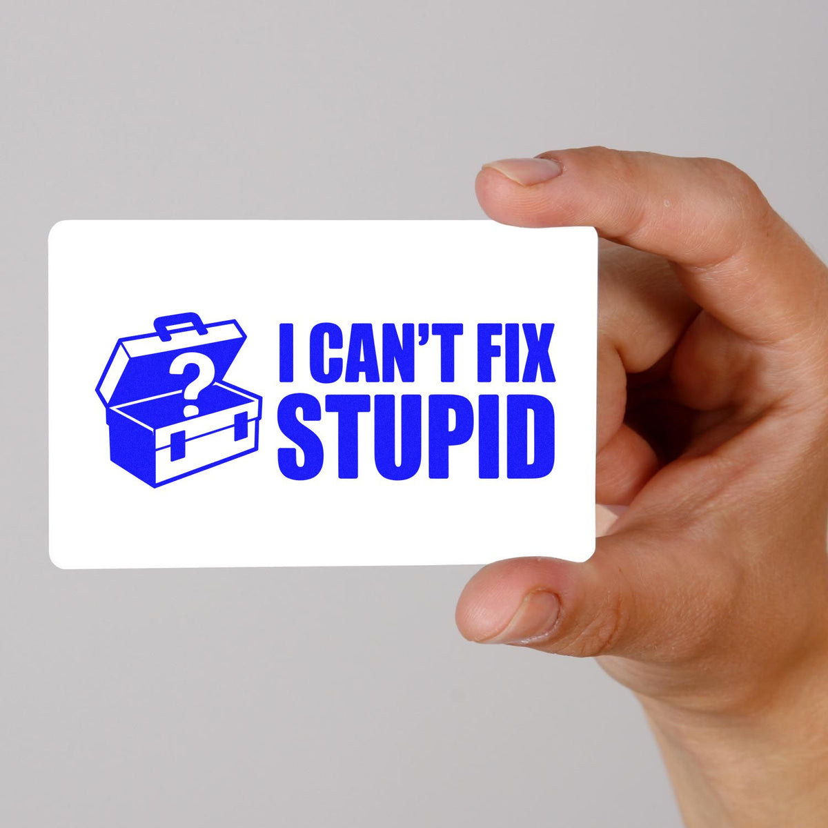Hand holding a novelty rubber stamp design featuring I CANT FIX STUPID with a blue toolbox icon.
