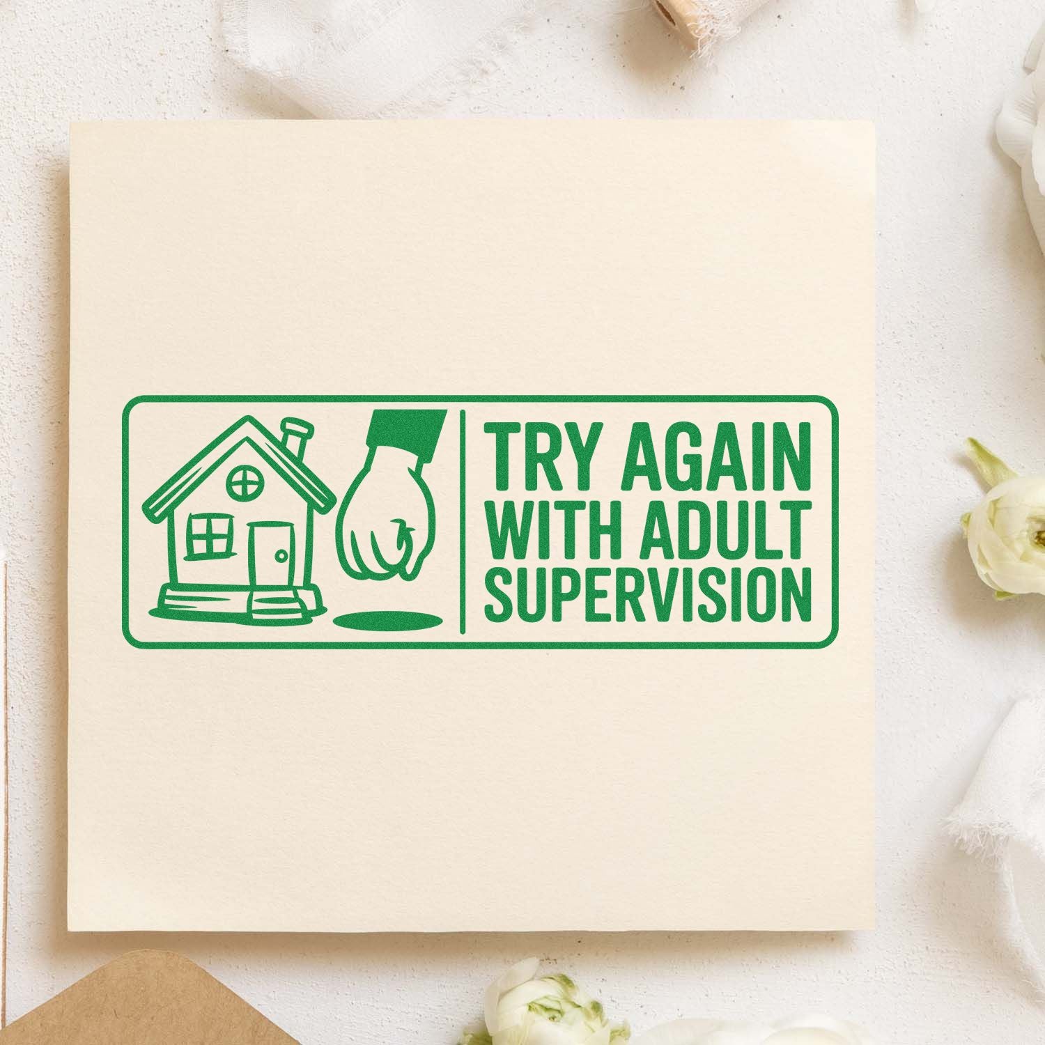 Green novelty rubber stamp reading Try Again With Adult Supervision with house and hand icon on paper.