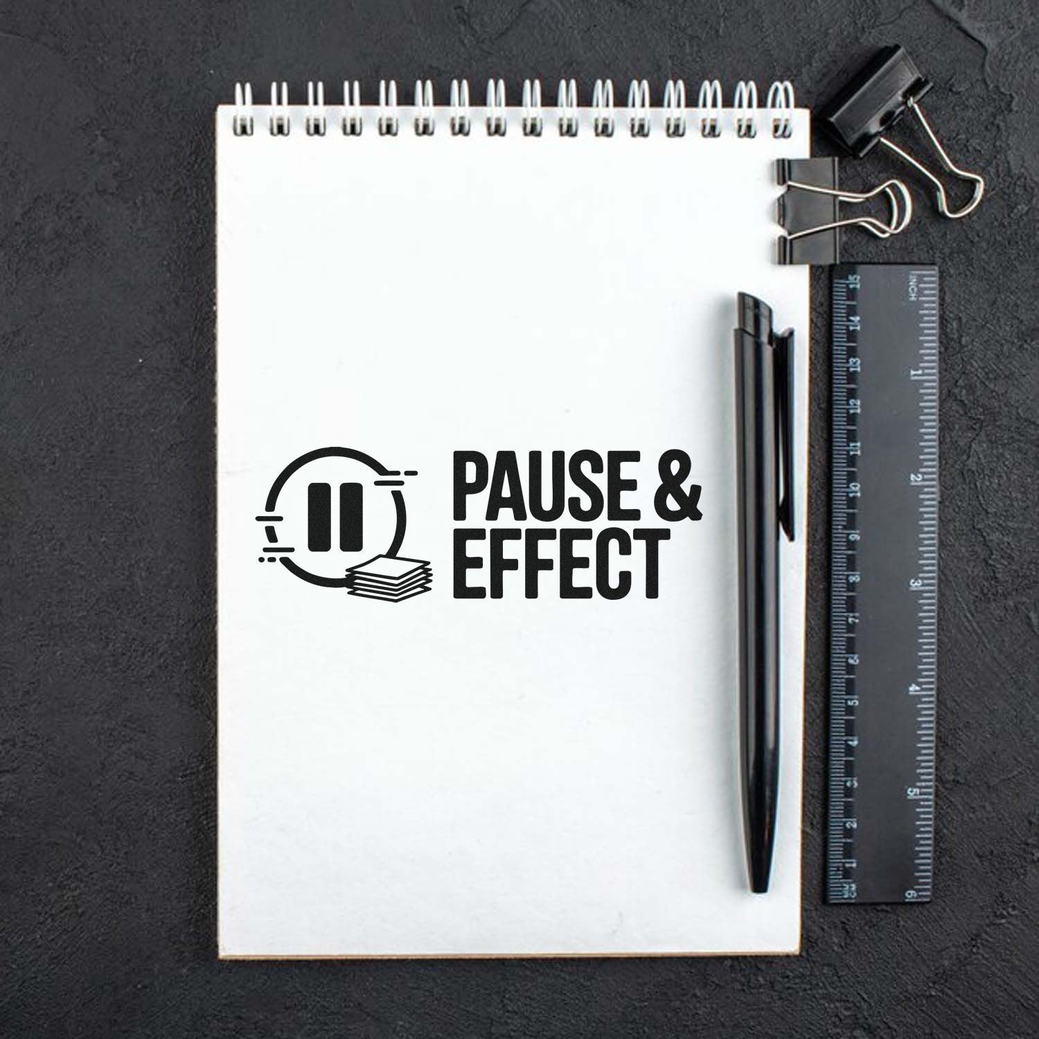 Pause & Effect rubber stamp design on a spiral notebook with pen and ruler, ideal for office or creative stationery.
