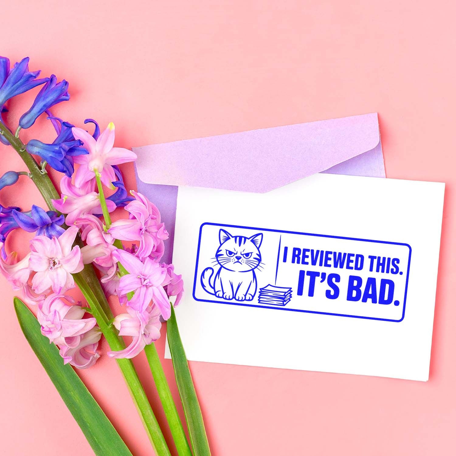 Funny cat rubber stamp mockup reading I reviewed this. Its bad. on a card beside flowers and envelope.