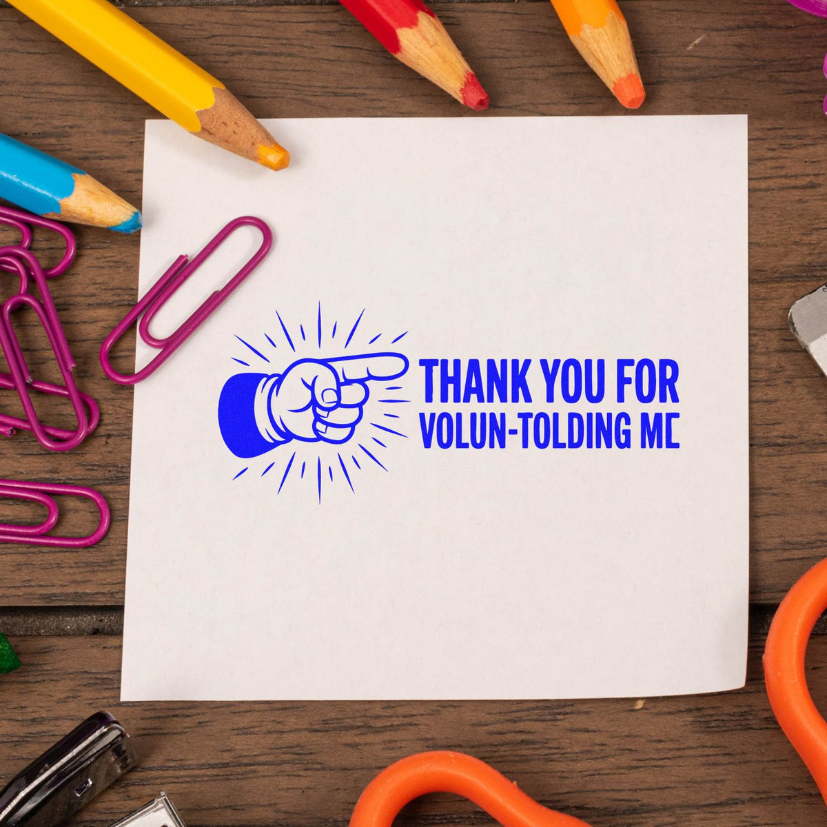Volunteer thank-you rubber stamp with pointing hand and bold blue Thank You for Volun-tolding Me message on paper.