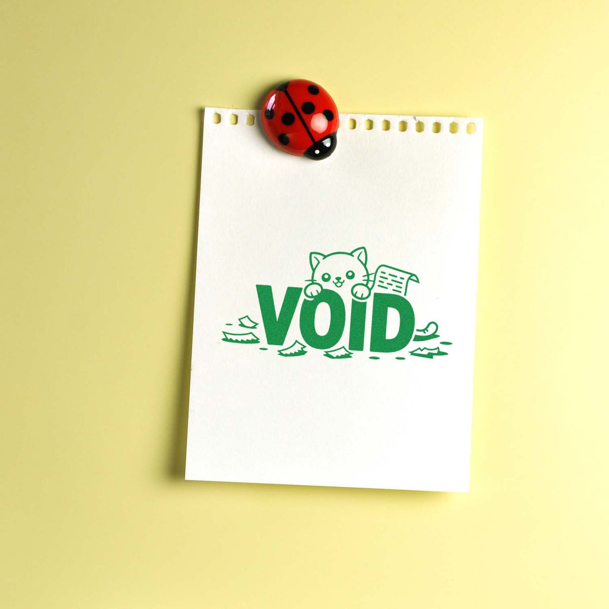 Green VOID rubber stamp imprint with cat design on notepad, pinned by ladybug magnet.