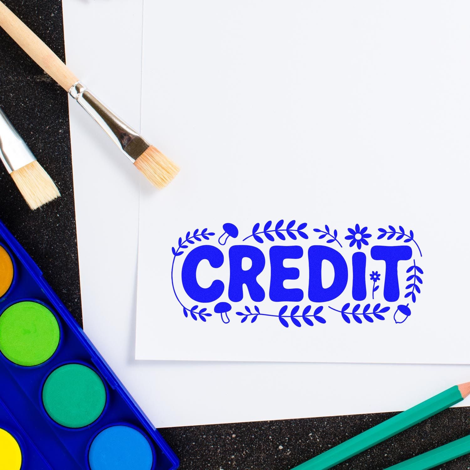 Custom CREDIT rubber stamp design on paper with art supplies for DIY crafts and stationery.
