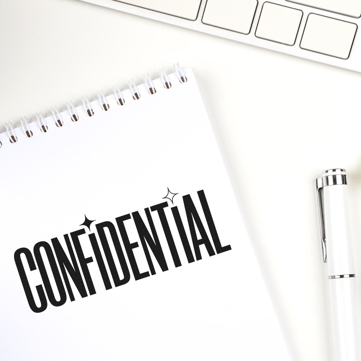 Confidential rubber stamp imprint on notebook, with pen and keyboard, for office document security and labeling.