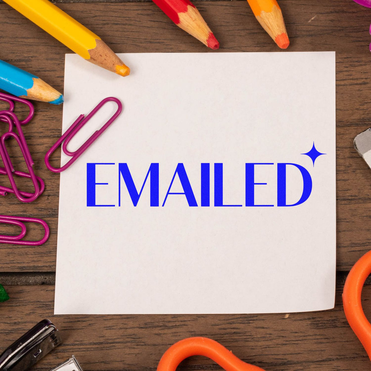 Blue Emailed rubber stamp impression on white paper with pencils and paper clips, ideal for office mail tracking.