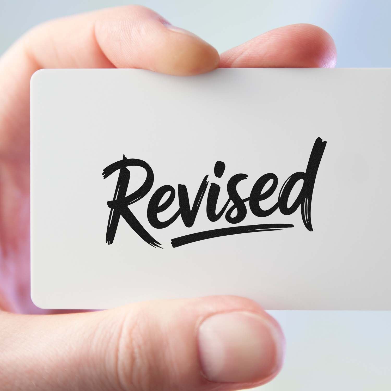 Hand holding a card with a Revised rubber stamp for document review and approval.