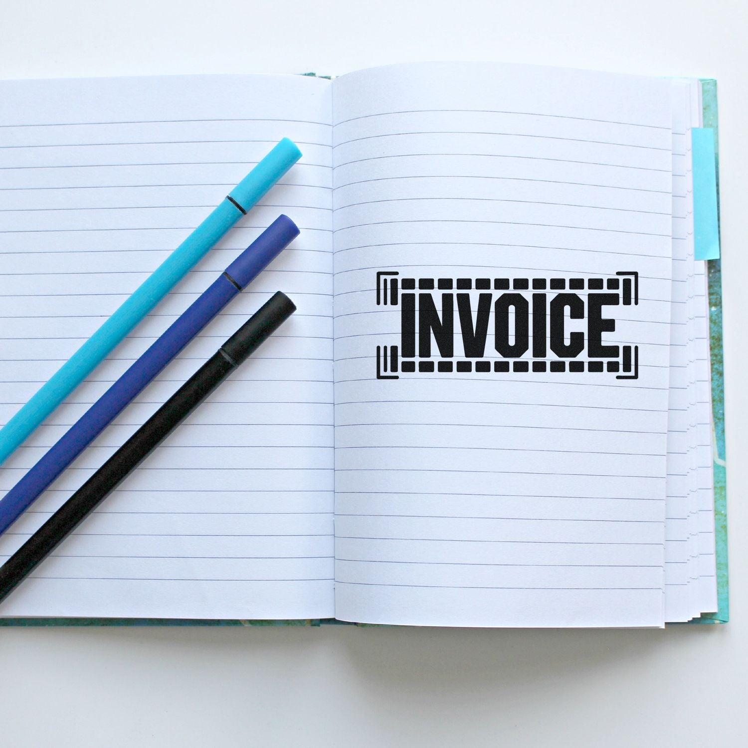 Invoice rubber stamp on open lined notebook with pens, ideal for accounting, billing, and office paperwork.