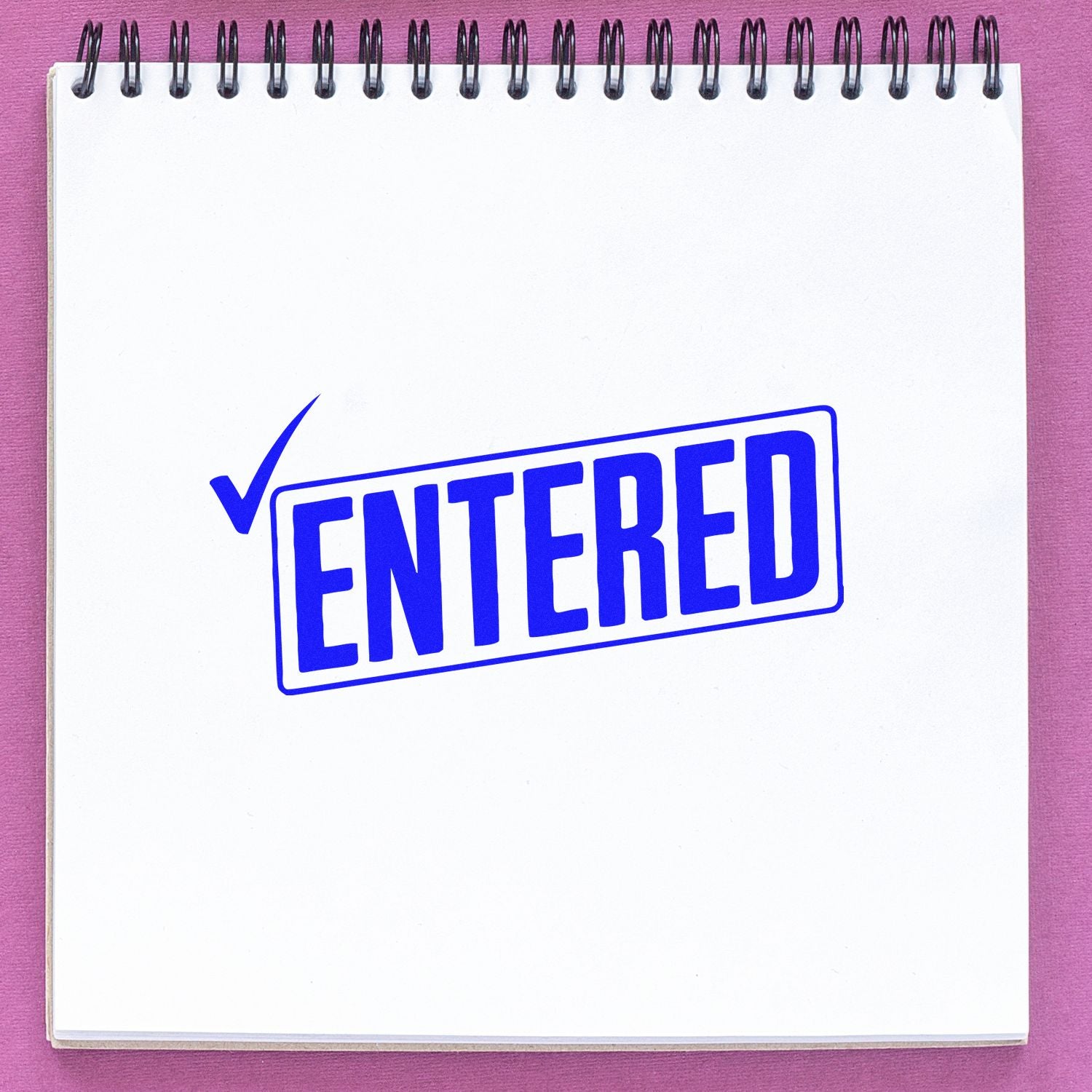 Blue ENTERED rubber stamp with check mark on notebook page for document approval, filing, or receipt processing.