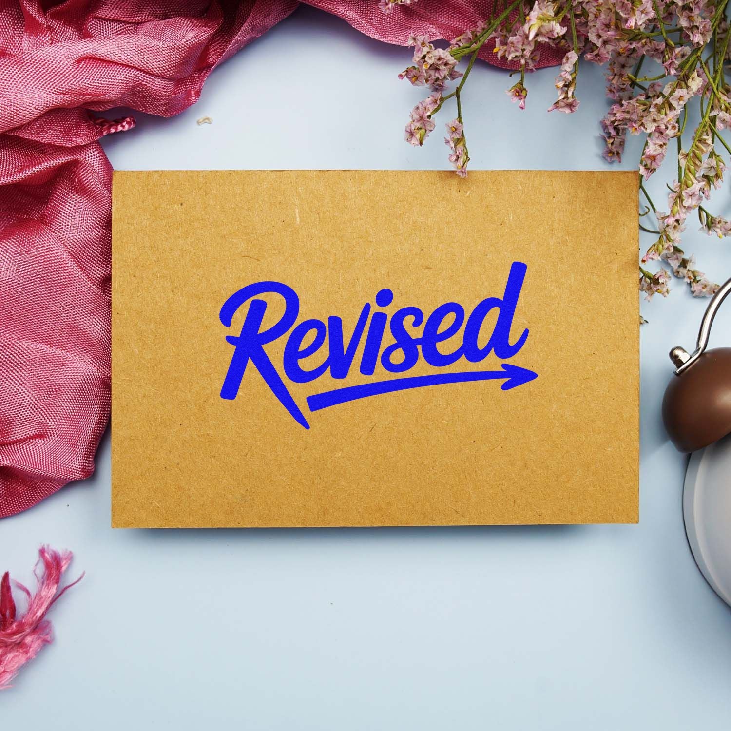 Blue Revised rubber stamp impression on kraft paper for marking edited documents and office paperwork.