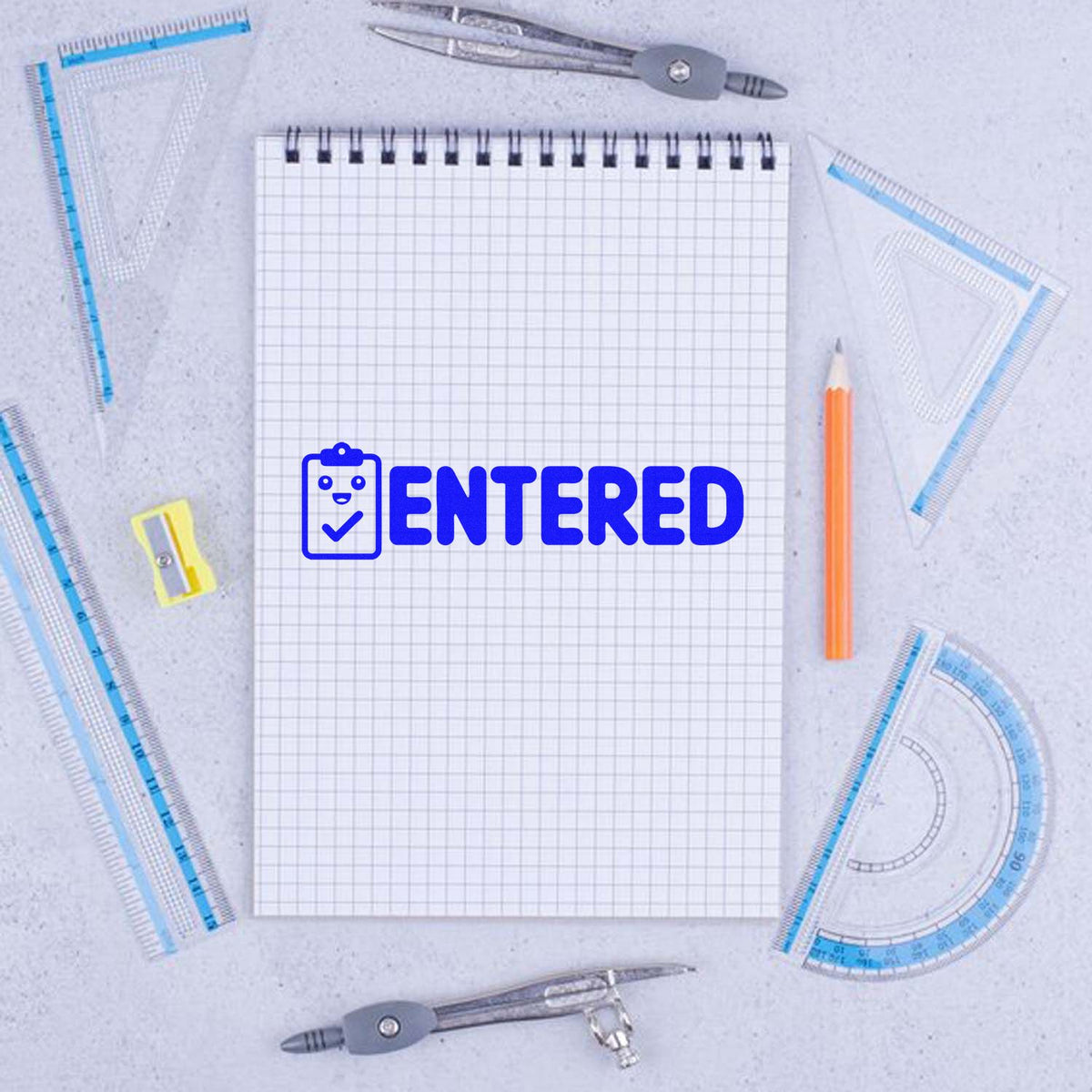 Blue ENTERED rubber stamp on graph paper notebook with geometry tools, ideal for school grading and office records.