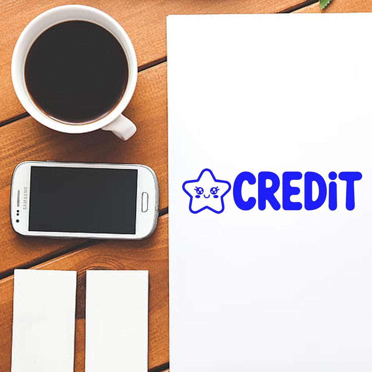 Blue credit rubber stamp on blank paper beside coffee and phone, ideal for office bookkeeping and document marking.