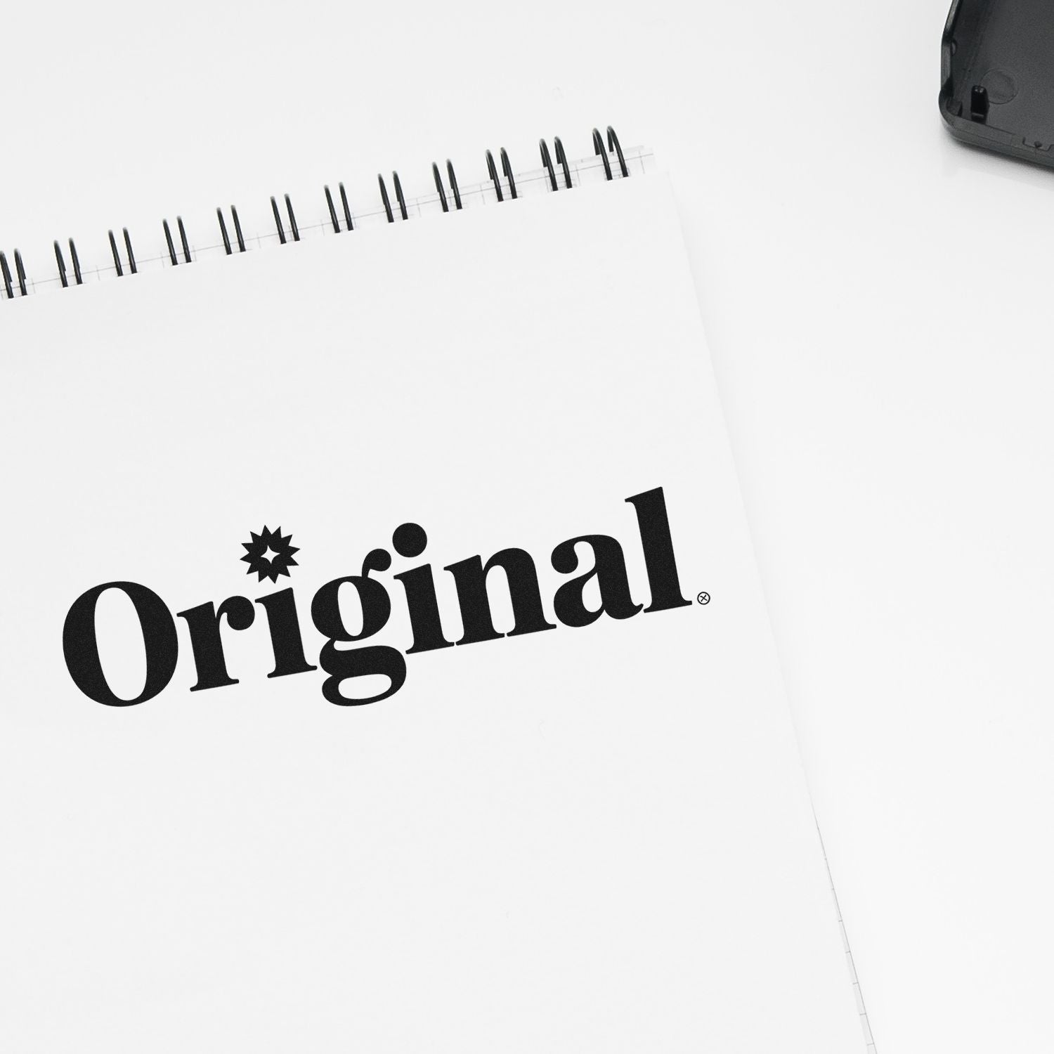 Original rubber stamp logo on spiral notebook, ideal for custom branding and stationery packaging.