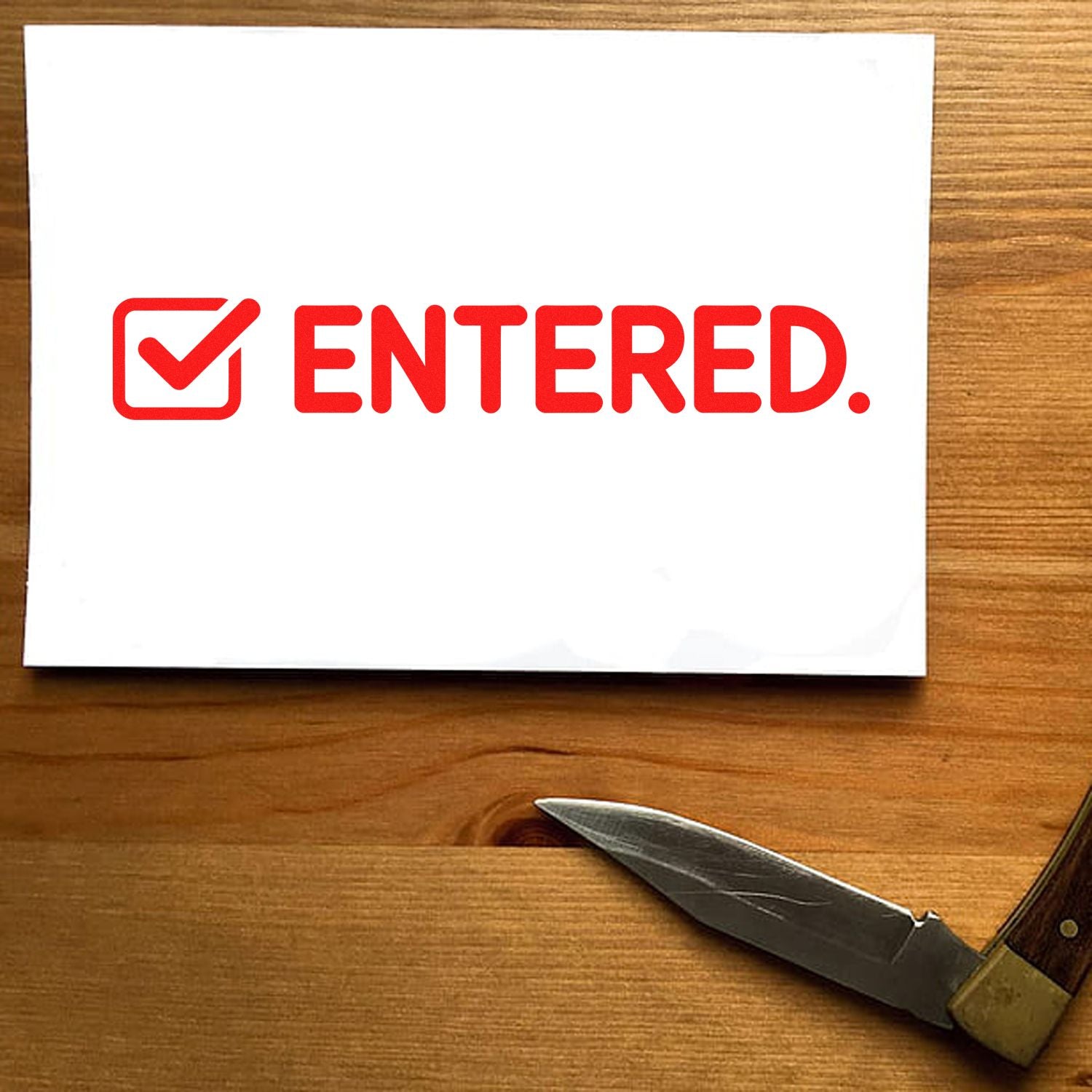 Red ENTERED rubber stamp with checkmark on paper for office document tracking, filing, and approval.