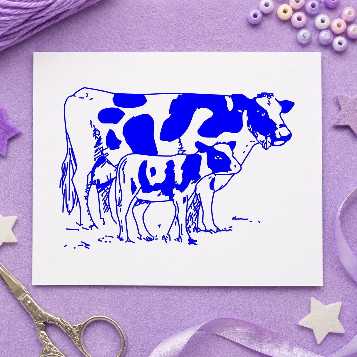 Mother Cow and Calf Rubber Stamp impression in blue ink on white paper in a styled craft setting.