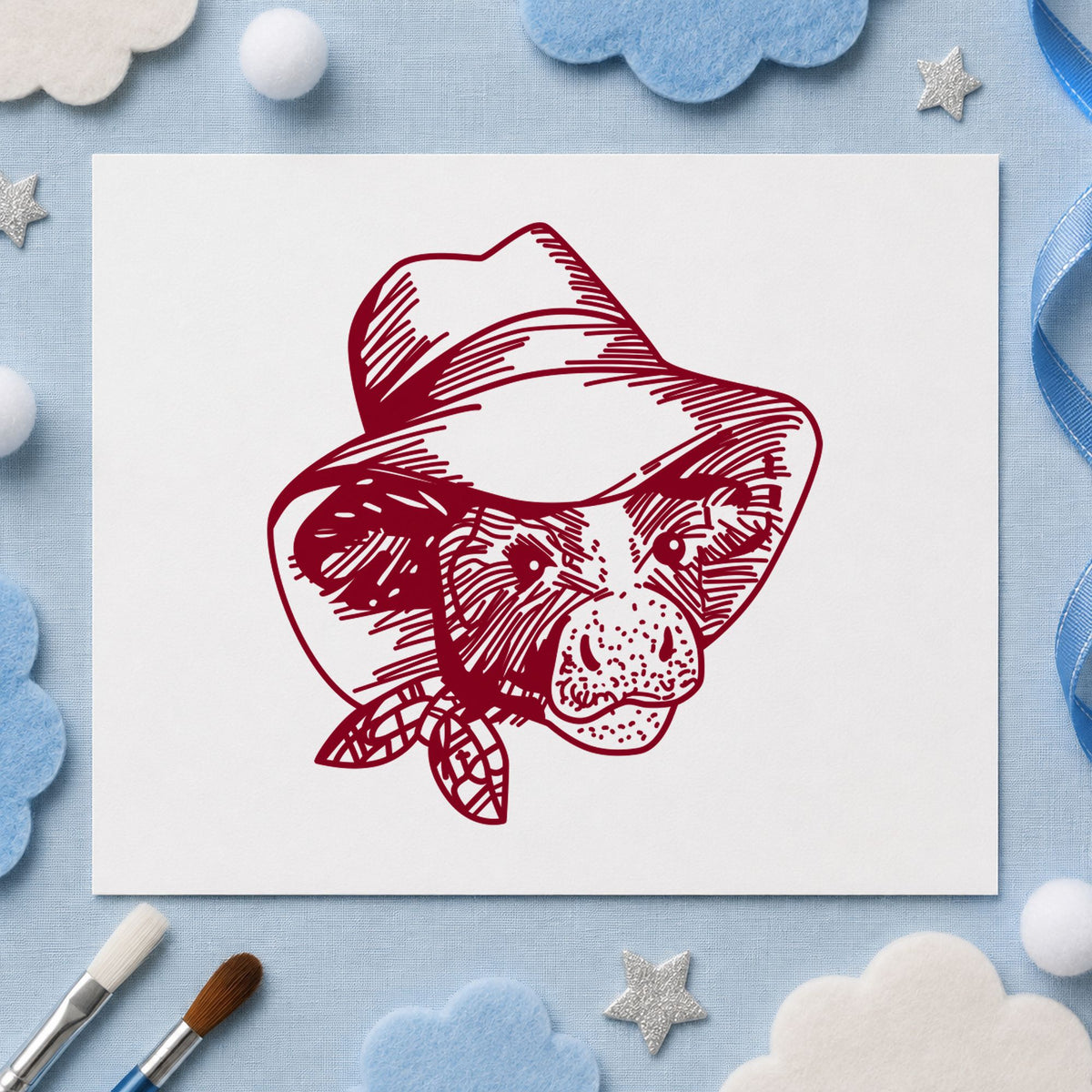 Cow in Cowboy Hat Rubber Stamp impression in burgundy ink on white paper in a styled craft setting.
