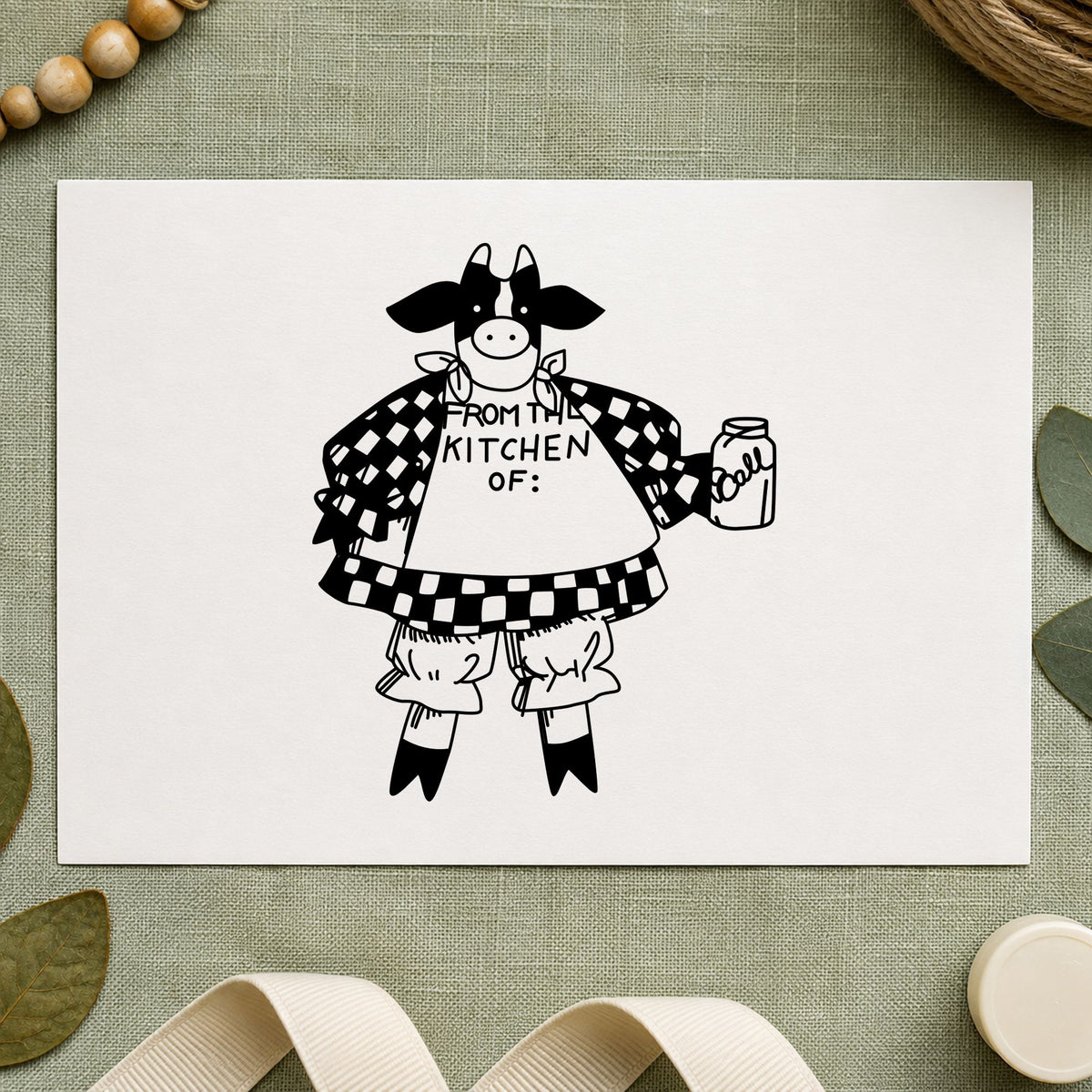 From the Kitchen Of Cow Rubber Stamp impression in black ink on white paper in a styled craft setting.